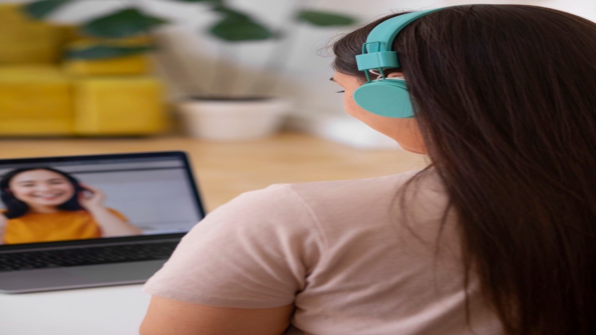 Usuário com fones turquesa em chamada de vídeo pelo notebook, com ambiente doméstico ao fundo